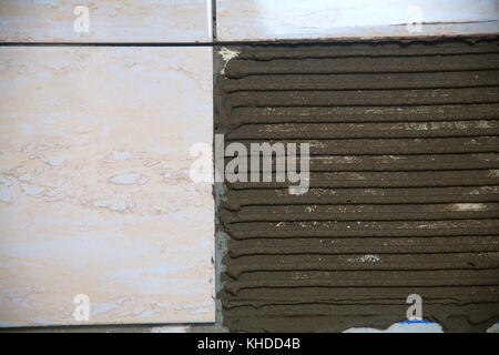 industrial construction worker installing small ceramic tiles on bathroom walls and applying mortar with trowel Stock Photo