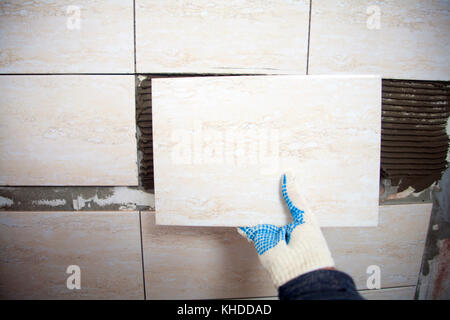 industrial construction worker installing small ceramic tiles on bathroom walls and applying mortar with trowel Stock Photo