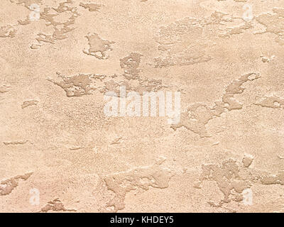 Old light brown wall covered with shabby peeling plaster. Texture of vintage bronze stone surface, closeup. Stock Photo