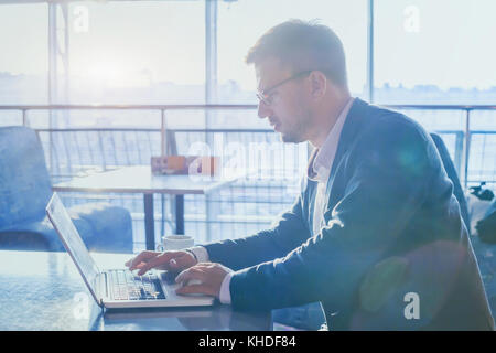 businessman working on computer in modern interior of airport cafe, man using internet on laptop, typing email, online banking concept Stock Photo