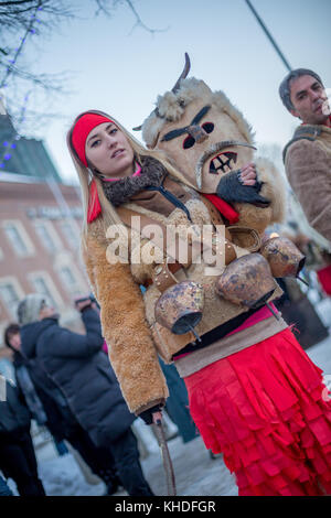 PERNIK, BULGARIA - JANUARY 27, 2017: Beautiful kuker girl carrying big brass ritual bells is holding her scary mask at Surva, the International Festiv Stock Photo