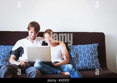 young couple looking at computer and smiling, family sitting on the couch at home Stock Photo