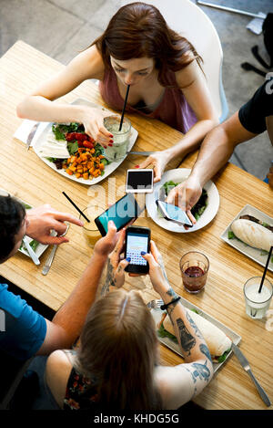 Group of friends sitting together in restaurants, all looking at smartphones Stock Photo