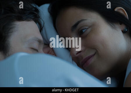 Young woman lying in bed looking at boyfriend sleeping Stock Photo