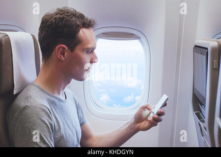 passenger using mobile phone smartphone in the airplane, wifi connection in plane during flight Stock Photo