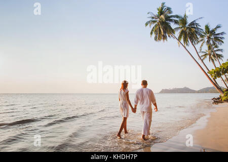 romantic young couple walking together on beautiful exotic tropical beach at sunset Stock Photo