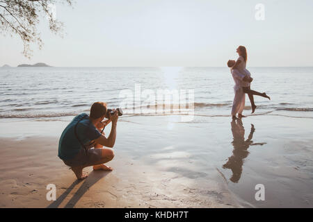 wedding and lifestyle photographer taking photos of affectionate couple on the beach at sunset Stock Photo