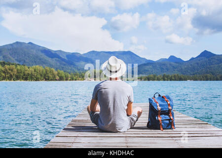 summer travel, young romantic man tourist wanderlust sitting on wooden pier Stock Photo