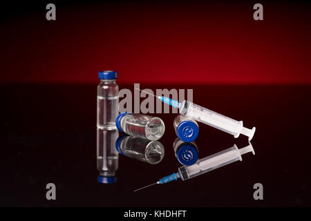 Syringe and medical vials isolated on red dark background with glossy reflection Stock Photo
