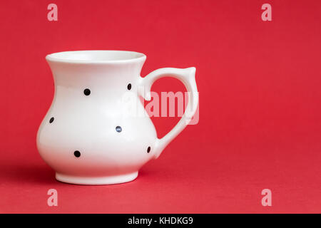 Close up of white vintage buttermilk cup with black dot pattern on red background Stock Photo
