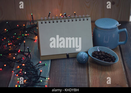 Open notebook, blue cup and coffee beans on Christmas table  Stock Photo