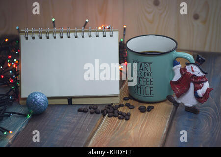 Open notebook, blue cup and Christmas toy snowman on the table   Stock Photo