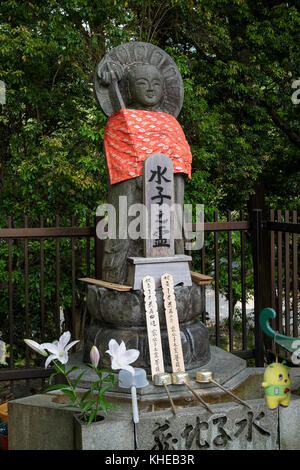 Nara, Japan -  May 31, 2017: Peaceful stone relegious Jizo statue with red skirt and a purification basin with ladles Stock Photo