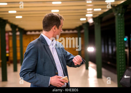A middle age businessman standing and waiting in the subway while talking on his phone and checking his watch Stock Photo