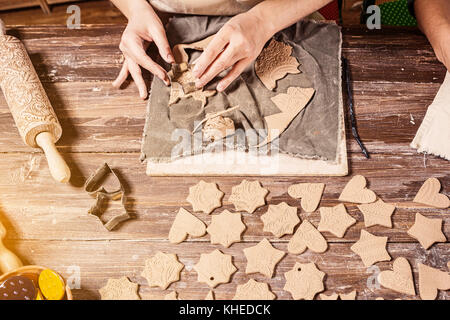 Close-up, two female potters make a lot of Christmas toys with the help of forms a Christmas tree made of brown clay, shaped like hearts, stars, bears Stock Photo