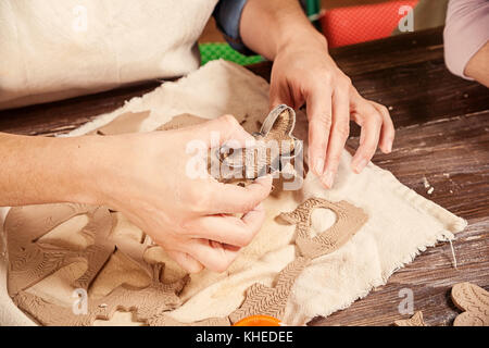 A close-up of a female potter makes a lot of Christmas toys with the help of forms a Christmas tree made of brown clay, shaped like hearts, stars, bea Stock Photo