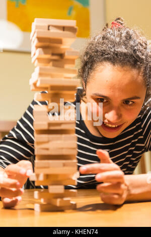 Young woman plays Jenga, stacking a tower with wooden blocks, concentrated Stock Photo
