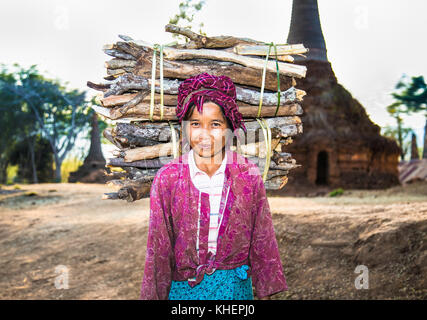 INLE, MYANMAR - MARC 4, 2017: Burmese woman carrying a bundle of heavy wood wearing traditional clothing on March  4, 2017, in Indein village , Myanma Stock Photo
