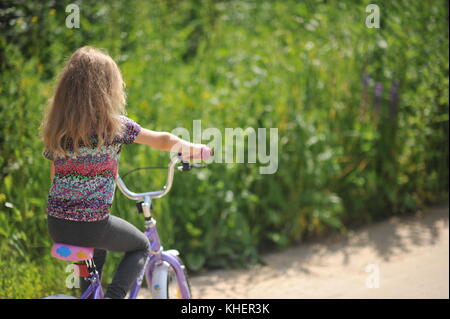 The girl was riding on a rural road on a bike in a field on a background of green vegetation Stock Photo