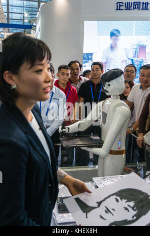 Intelligent AI drawing robot sketching pictures likenesses of people, woman holding portrait just sketched by robot, at China hi-tech fair in Shenzhen, known as 'Silicon Valley of China', Shenzhen, China. Stock Photo
