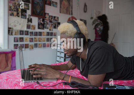 Young man listening to headphones while using his laptop on his bed Stock Photo
