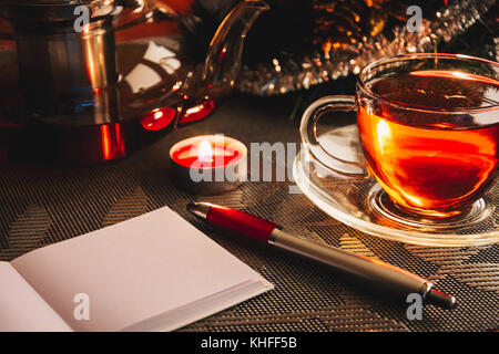 Wish list notepad with blank page on the table near christmas tree, cup of tea, teapot and candle. Letter to Santa Claus Stock Photo