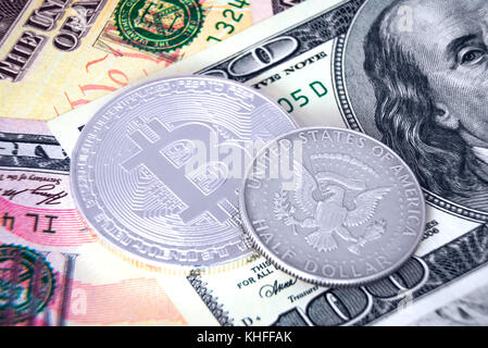 Silver bitcoin and 50 cent coin laying on dollar banknotes Stock Photo