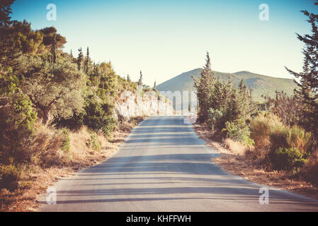 Long road leading towards through the mountains. Sunset. Summer. Long shadows. Vintage photo Stock Photo