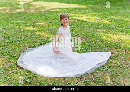 Beautiful bride in white lace dress sitting on green grass Stock Photo