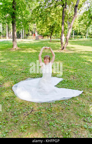 Bride in white lace dress with upwards hands sitting on the grass Stock Photo