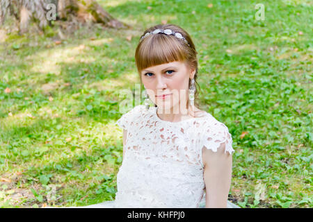 Beautiful bride in white dress sitting on the green grass Stock Photo