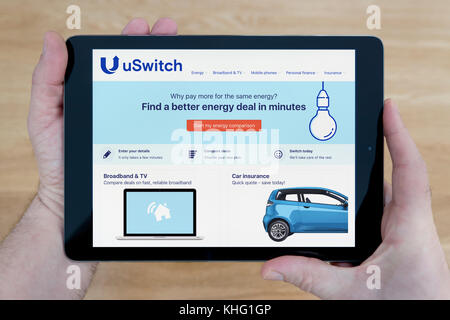 A man looks at the uSwitch website on his iPad tablet device, shot against a wooden table top background (Editorial use only) Stock Photo
