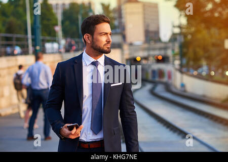 A handsome young businessman standing and waiting at the tramstop in the sunset Stock Photo