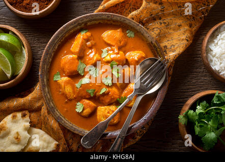 A bowl of delicious indian butter chicken curry with naan bread, basmati rice, and cilantro garnish. Stock Photo