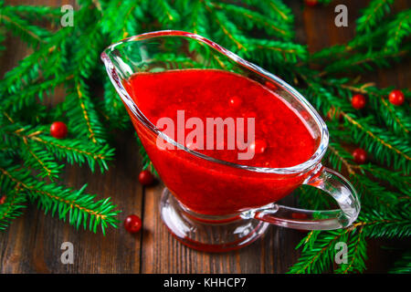 Cowberry cranberry sauce in a glass clear saucer on a wooden table with spruce branches Stock Photo