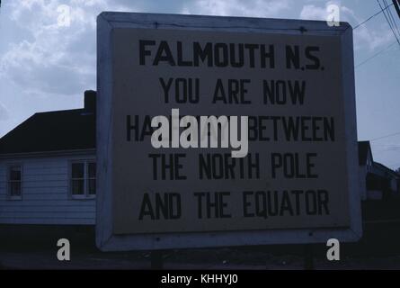 A photograph of a sign in Falmouth stating that it is placed halfway between the equator and the north pole, homes can be seen in the background, Nova Scotia, Canada, 1961. Stock Photo