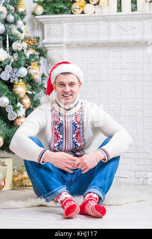 nice man in a sweater and New Year's socks sitting near a Christmas tree Stock Photo
