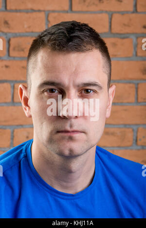 portrait of brutal brunette in blue t-shirt on brick wall background Stock Photo