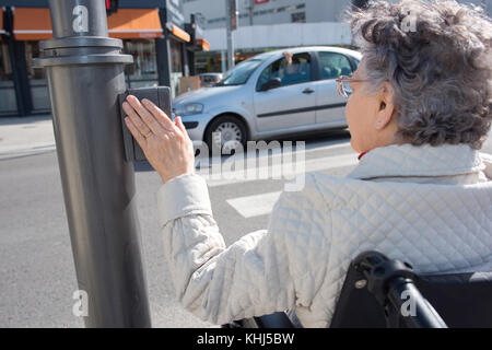 senior female on a wheelchair pushing button for traffic light Stock Photo