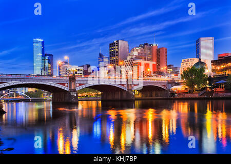 Princes bridge over Yarra river in Melbourne city CBD at sunrise when bright illumination lights reflect in blurred water. Stock Photo