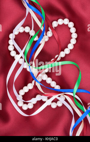 Hearts made of white beads and multi-colored ribbons lying on red silk View from above Stock Photo
