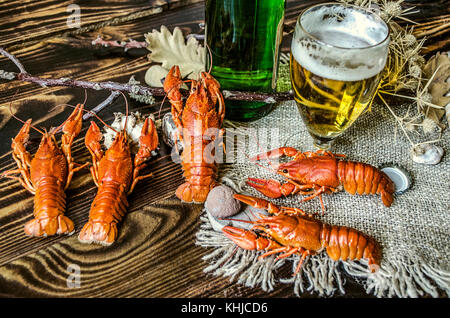 Half-empty glass with beer and a bottle of beer and salted boiled red crayfish on canvas lying on dark wooden boards Stock Photo