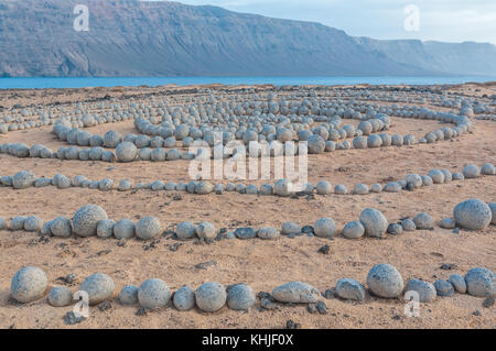 completely circular stones on the ground forming a spiral near the beach, with Lanzarote in the background, Caleta del Sebo, La Graciosa, Canary Islan Stock Photo