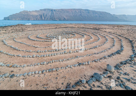 completely circular stones on the ground forming a spiral near the beach, with Lanzarote in the background, Caleta del Sebo, La Graciosa, Canary Islan Stock Photo