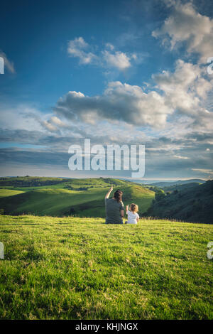 Mother Wth Daughter Sitting on Grass and Admiring Clouds Stock Photo