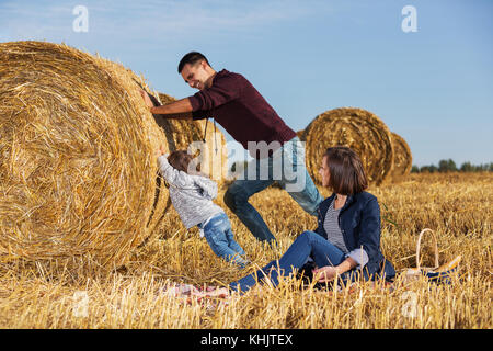 Happy young father and his 2 year old girl pushing a hay bale in harvested field Stock Photo