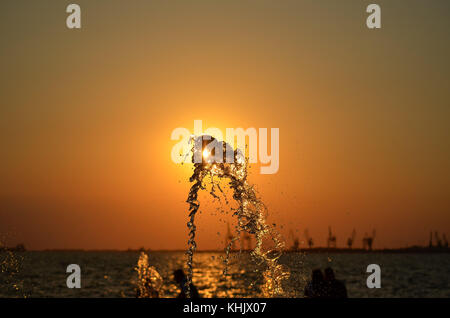 Water splash isolated on sunset colors background with people and cranes silhouettes. Stock Photo