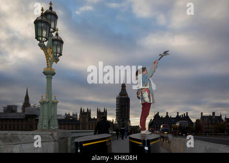 With the winter landscape of Westminster and the Houses of Parliament on the river Thames opposite, a woman with a David Bowie bag stands on the anti-terrorism security barriers at the southern end of Westminster Bridge, to take a picture of the London Eye, on 8th November 2017, in Lambeth, London. Stock Photo