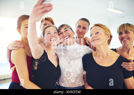 Mixed age group of laughing women standing arm in arm together taking a selfie during ballet class Stock Photo