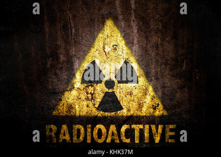 Yellow radioactive (ionizing radiation) danger symbol with word radioactive painted below the sign on a massive concrete wall with dark rustic grunge  Stock Photo